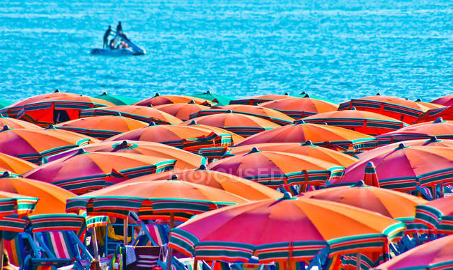 Sun umbrellas on beach with a boat in the distance, Italy — Stock Photo