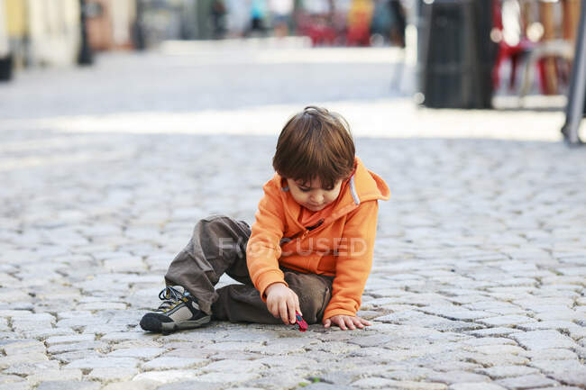 Niño sentado en la calle jugando con coche de juguete - foto de stock