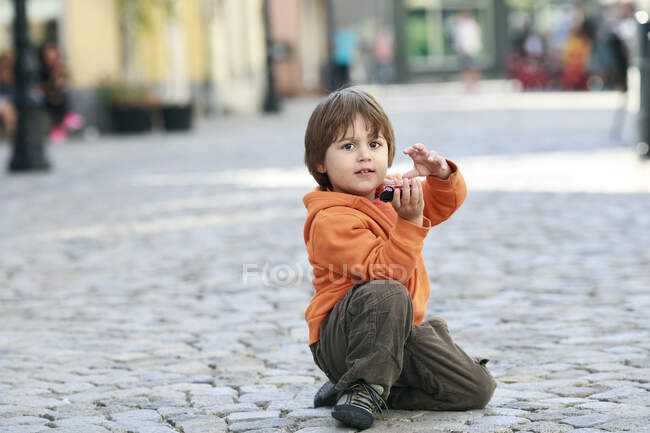 Boy sitting in street playing with toy car — Stock Photo