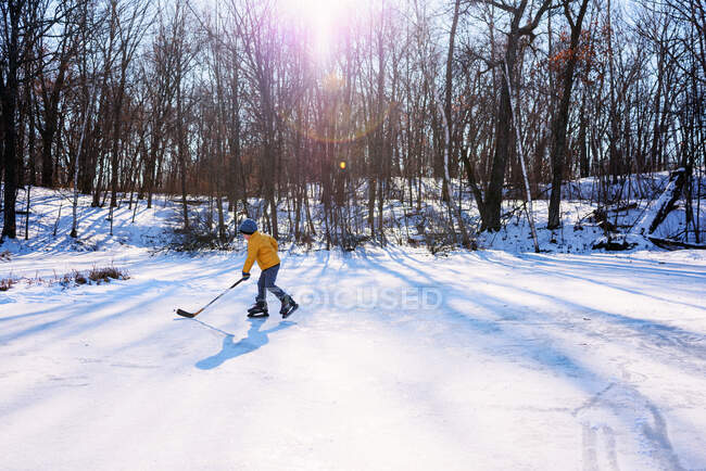 Boy playing ice hockey on ice rink on nature — Stock Photo