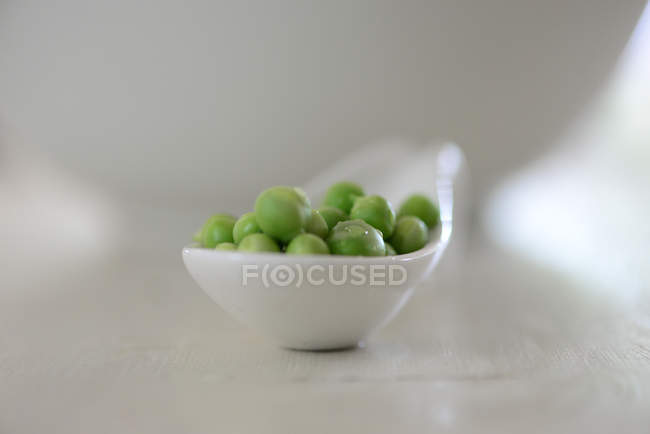 Closeup view of white spoon with peas — Stock Photo