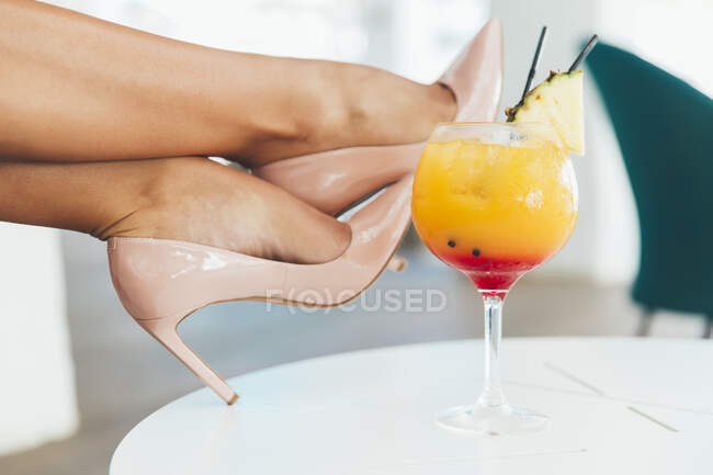 Жінка торкається її щиколотки на столі з коктейлем — стокове фото