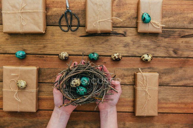 Presentes embrulhados e mãos de menina segurando um ninho com ovos de Páscoa — Fotografia de Stock