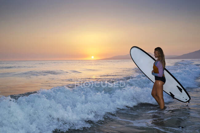 Женщина, идущая в океан с доской для серфинга, пляж Лос Лансес, Тарифа, Кадис, Андалусия, Испания — стоковое фото