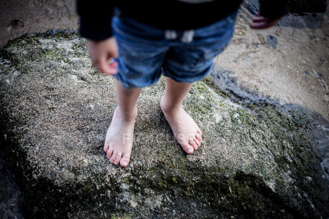 Garçon debout pieds nus sur des rochers humides — Photo de stock
