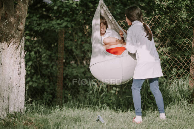 Girl pushing a boy sitting in a hanging chair — Stock Photo