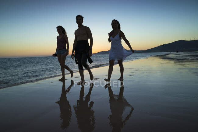 Silhouette de trois personnes marchant le long de la plage au coucher du soleil, plage de Los Lances, Tarifa, Cadix, Andalousie, Espagne — Photo de stock