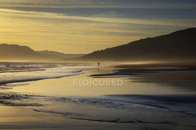 Silhouette einer Person, die bei Sonnenuntergang am Strand entlang geht, los lances beach, tarifa, cadiz, andalucia, spanien — Stockfoto