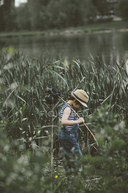 Junge läuft am Fluss entlang und trägt Binde am Stock — Stockfoto