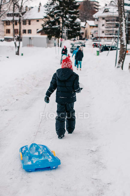 Мальчик тянет сани на зимней улице — стоковое фото