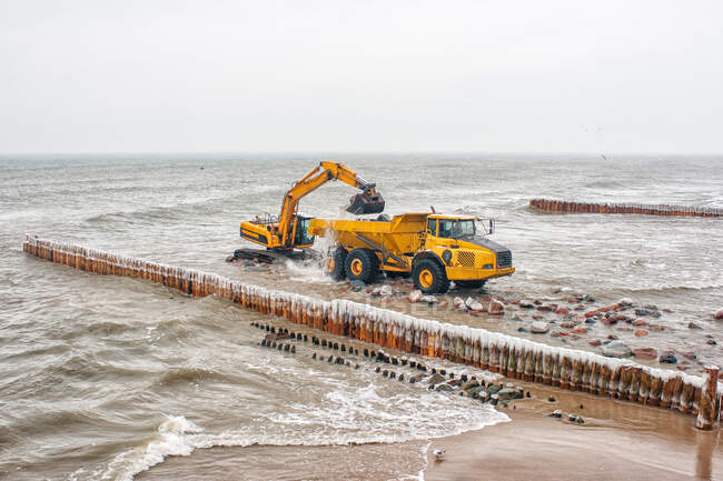 Camión excavador cargando piedras en un camión en la playa, Mar Báltico, Kaliningrado, Federación Rusa - foto de stock