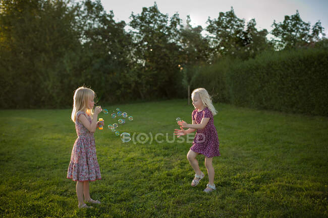 Duas meninas soprando bolhas no jardim — Fotografia de Stock