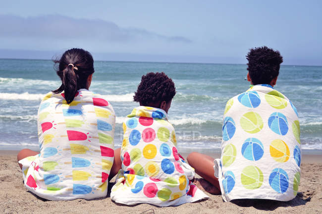 Três meninas sentadas na praia envoltas em toalhas — Fotografia de Stock