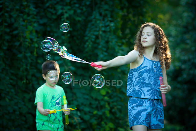 Chico y chica soplando burbujas de jabón gigante - foto de stock