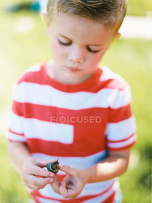 Хлопчик тримає равлика на зеленому лузі — стокове фото