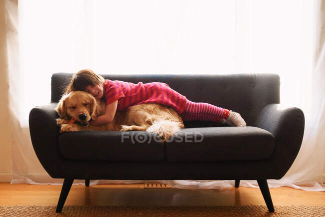 Девочка лежит на диване со своей золотой собакой-ретривером — стоковое фото