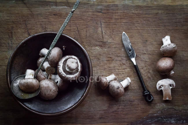 Mushrooms in bowl and on wooden table, top view — Stock Photo