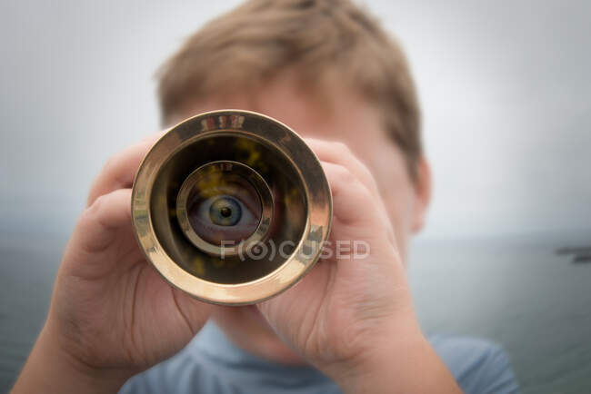 Rapaz parado junto ao mar a olhar através de um telescópio — Fotografia de Stock