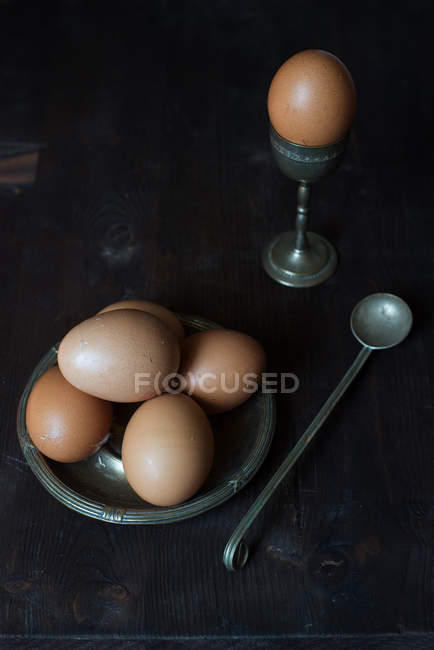 Metal egg cup and eggs over vintage table — Stock Photo