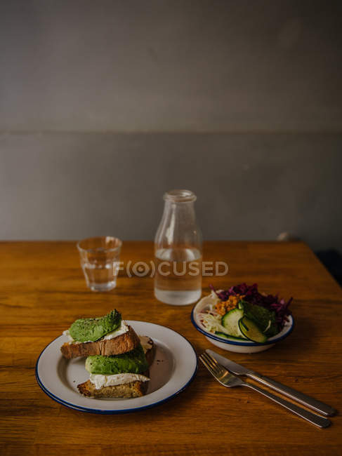 Cream cheese and avocado toast with salad and water — Stock Photo