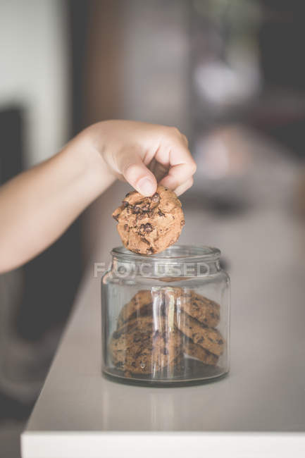 Ragazzo mano raccogliendo un biscotto al cioccolato da un barattolo di vetro — Foto stock