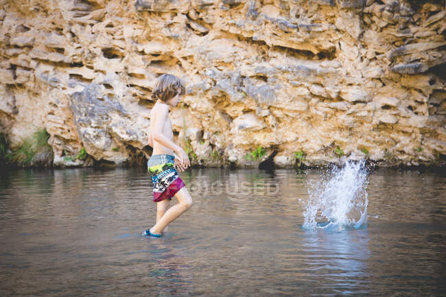 Boy throwing stones in the river on nature — Stock Photo