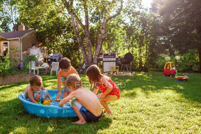 Cuatro niños jugando afuera en una piscina infantil en el jardín - foto de stock