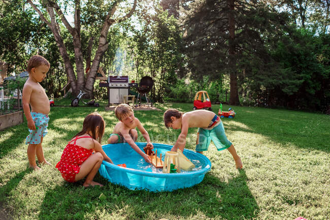Quatro crianças brincando fora em uma piscina de remo no jardim — Fotografia de Stock