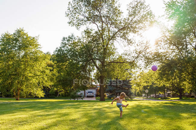 Chico de pie en el jardín pateando una pelota - foto de stock