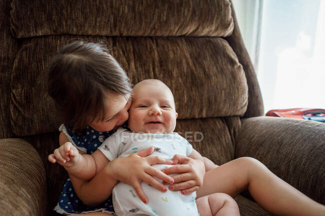 Fille assise sur une chaise câlinant un bébé garçon — Photo de stock