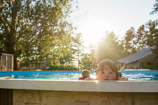 Мальчик смотрит через край бассейна с братьями и сестрами на заднем плане — стоковое фото