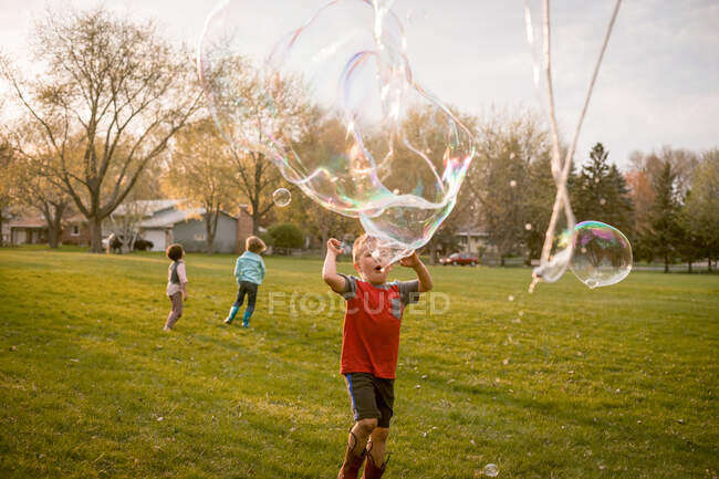 Tres niños jugando con burbujas gigantes en un parque - foto de stock