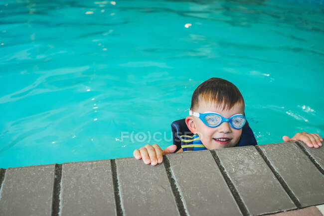 Boy wearing swimming goggles peeking over the edge of a swimming pool — Stock Photo