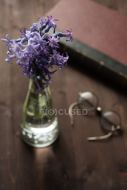Hyacinths in a vase, spectacles and an old book on a wooden table — Stock Photo