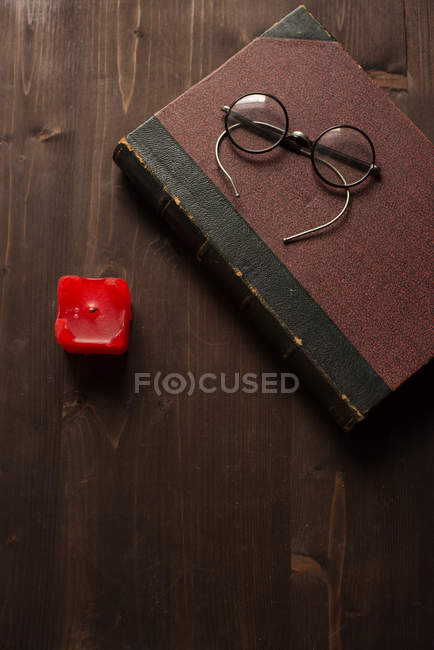 Livro velho, uma vela vermelha e espetáculos em uma mesa de madeira — Fotografia de Stock