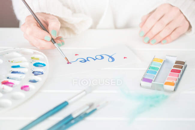 Mulher escrevendo a palavra amor em tinta aquarela — Fotografia de Stock