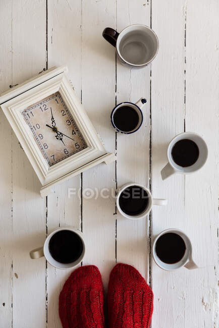 Frauenfüße im Stehen bei Uhr und Tassen Kaffee — Stockfoto