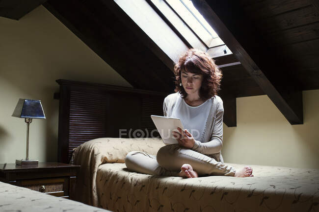 Жінка сидить на ліжку читає цифровий планшет — стокове фото