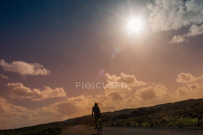 Fille vélo le long de la route au coucher du soleil — Photo de stock