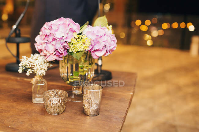 Flores en jarrones de vidrio con velas sobre mesa de madera - foto de stock