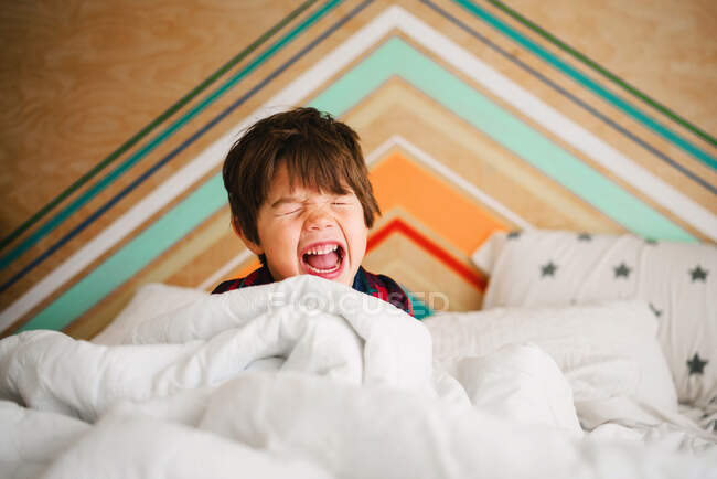 Мальчик сидит в постели и кричит: — стоковое фото