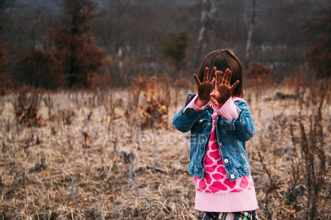 Chica de pie en el paisaje rural sosteniendo las manos sucias delante de su cara - foto de stock