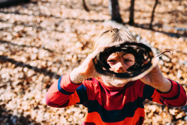 Boy looking through a roll of tree bark in the woods — Stock Photo