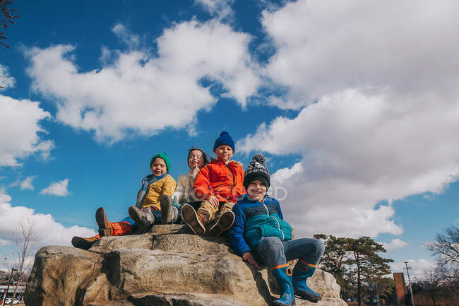 Four children sitting on the top of a climbing rock at a playground — Stock Photo