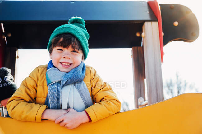 Мальчик в теплой одежде стоит на скалолазании на детской площадке — стоковое фото
