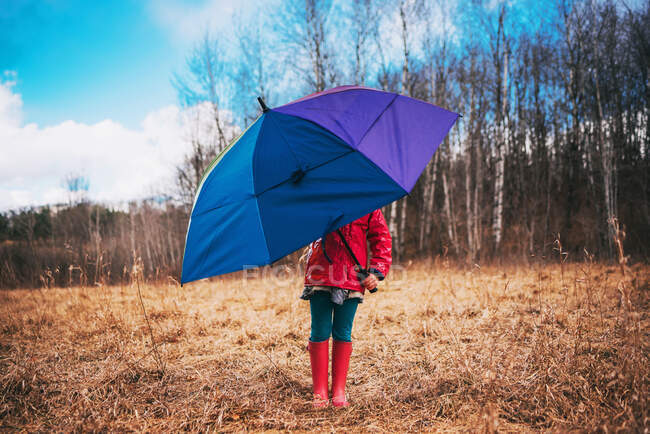 Mädchen steht in ländlicher Landschaft und hält einen bunten Regenschirm — Stockfoto