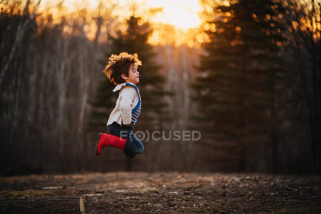 Boy jumping off a log in the forest — Stock Photo