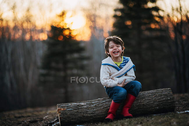 Мальчик сидит на бревне и смеется — стоковое фото