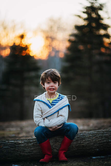 Garçon assis sur une bûche riant — Photo de stock