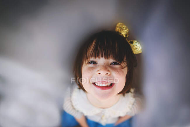 Ritratto di una ragazza sorridente con un fiocco che alza lo sguardo attraverso una tenda — Foto stock